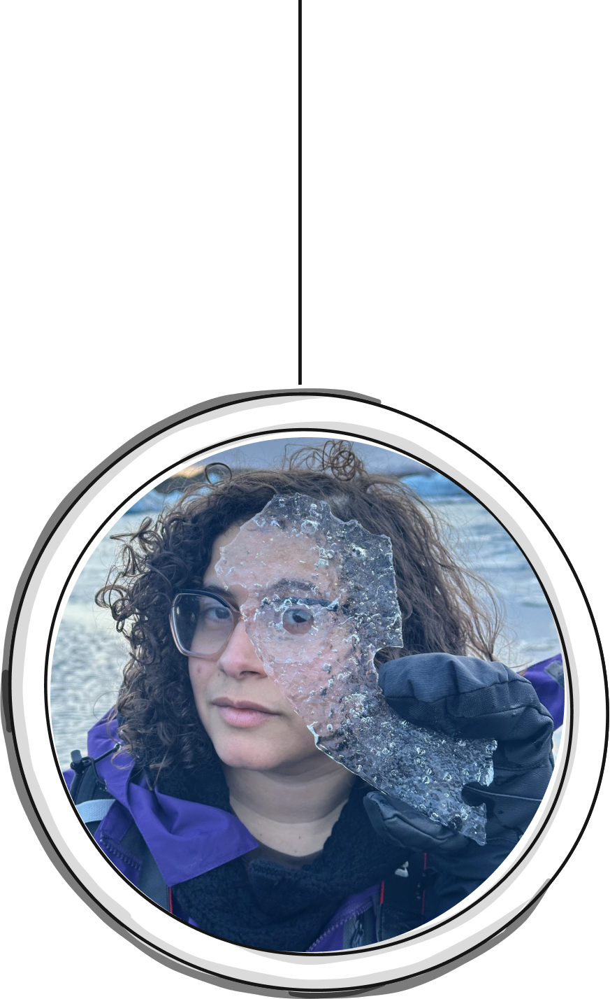 Image of Lissy wearing large glasses and a purple jacket holding up a piece of ice to their eye
